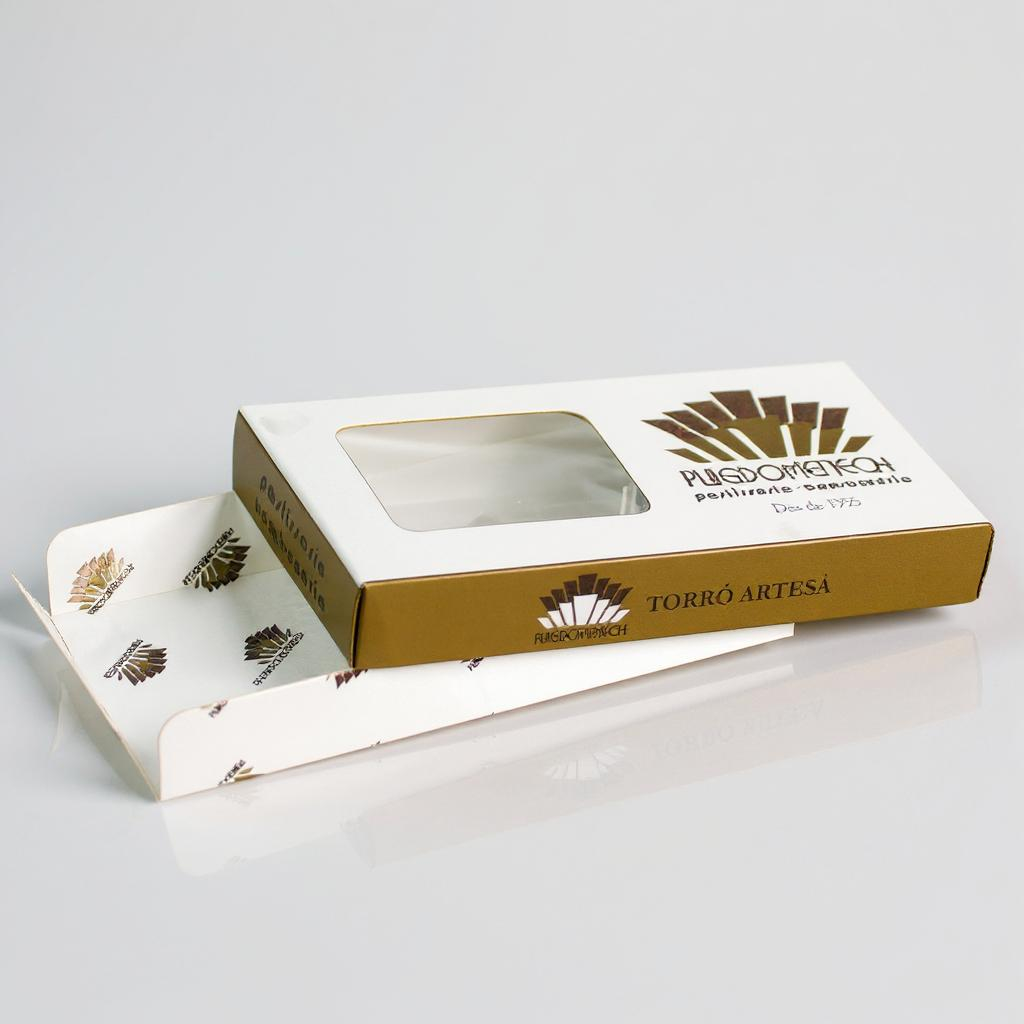 Caja de cartón blanca con detalles dorados para turrón artesano, con ventana transparente en la tapa y bandeja interior decorada, fotografiada sobre fondo blanco