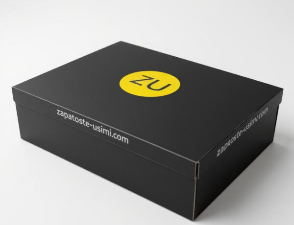 Caja de zapatos negra de cartón con logotipo amarillo ZU en la tapa y dirección web en los laterales, fotografiada sobre fondo blanco
